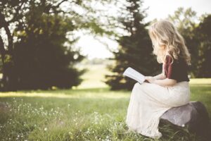 V záhrade sedí osamelá žena na kameni a číta knihu.